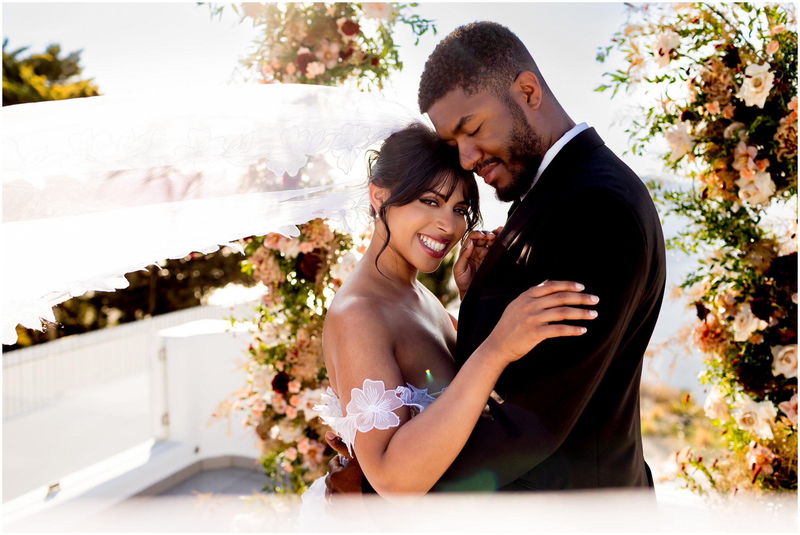 bride smiling at the camera whilst veil is blowing in the wind